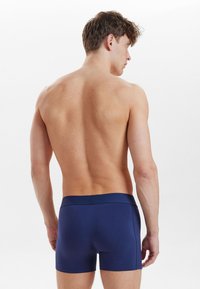 Boxer shorts blu navy con un morbido elastico in vita, design aderente e texture liscia, visti da dietro, evidenziando la forma e il profilo.