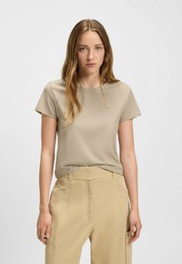 Beżowy t-shirt z krótkim rękawem z miękkiego materiału, z okrągłym dekoltem, z małym wytłoczonym logo na klatce piersiowej.