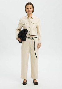 Beige denimjack en broeken, met een zwarte geweven tas, voorzien van een gevlochten riem. Eenvoudig ontwerp met een cropped jack en brede broekspijpen.