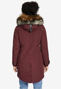 Parka burdeos con capucha forrada de pelo sintético, botones a presión, puños elásticos y una parte trasera ligeramente alargada para mayor cobertura.