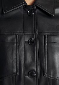 Chaqueta de cuero negro vista frontal con cuello, costuras visibles, dos bolsillos verticales en el pecho y tres grandes botones negros abrochados en el centro.