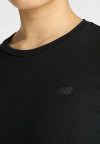 Schwarzes, geripptes Sportshirt mit rundem Halsausschnitt und einem dezenten grauen Logo auf der linken Seite. Glatte Textur.