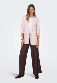 Ροζ ανοιχτόχρωμο λινό σακάκι με φαρδιά εφαρμογή και μανίκια τριών τετάρτων, από πάνω ενός λευκού τοπ. Σκούρο καφέ παντελόνι με φαρδιά μπατζάκια και γυαλιστερά μποτάκια αστραγάλου.