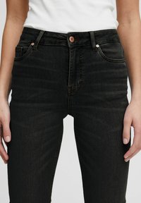 Jeans de algodón negro de tiro alto con una forma ajustada, con herrajes de botón en cobre, textura sutil y bolsillos frontales.