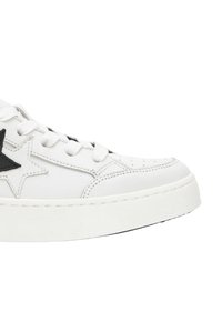 Sneaker bianco in pelle con accento a stella nera. Presenta punte rotonde, chiusura con lacci e suole in gomma testurizzata.