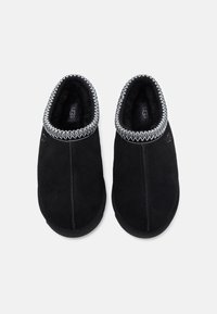 Chaussons en daim noir avec une bordure texturée, dotés d'un doublure douce et d'une forme arrondie. Détail de couture remarquable le long des bords.