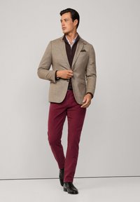 Beige blazer, bordeaux ritsvest, bordeaux broek en zwarte schoenen. De blazer heeft een notch-lapel en een borstzak. Glad textuur.