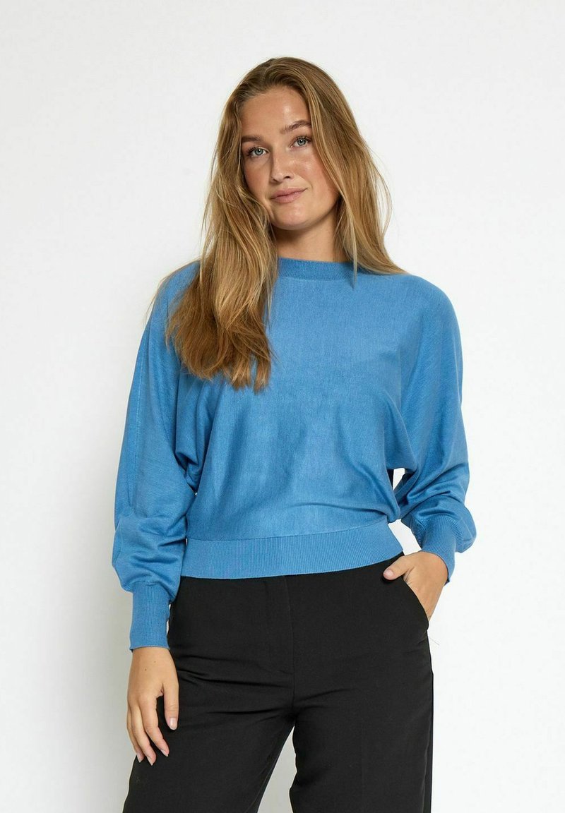 Maglione blu lavorato a maglia con scollatura rotonda, vestibilità ampia e orlo a coste. Abbinato a pantaloni neri. Texture liscia, design casual.