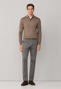 Lichtbruin lange mouwen pullover met een kraag en twee knopen, gecombineerd met slim-fit grijze broeken en bruine schoenen. Netjes, textuurstof.