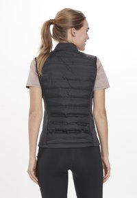 Svart puffig väst med hög krage och quiltad yta, kombinerad med en ljusrosa kortärmad topp, bärs över svarta leggings.