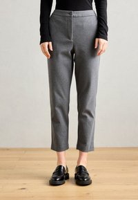 Grå skreddersydde bukser med rette bein, med knappelukking, flat front og oppbrettede hem, kombinert med svarte loafers på et tregulv.