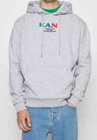 Felpa grigia con tasca a kangaroo, cordini, e logo testuale colorato sul petto. Tessuto morbido, vestibilità comoda, polsini e orlo a coste.