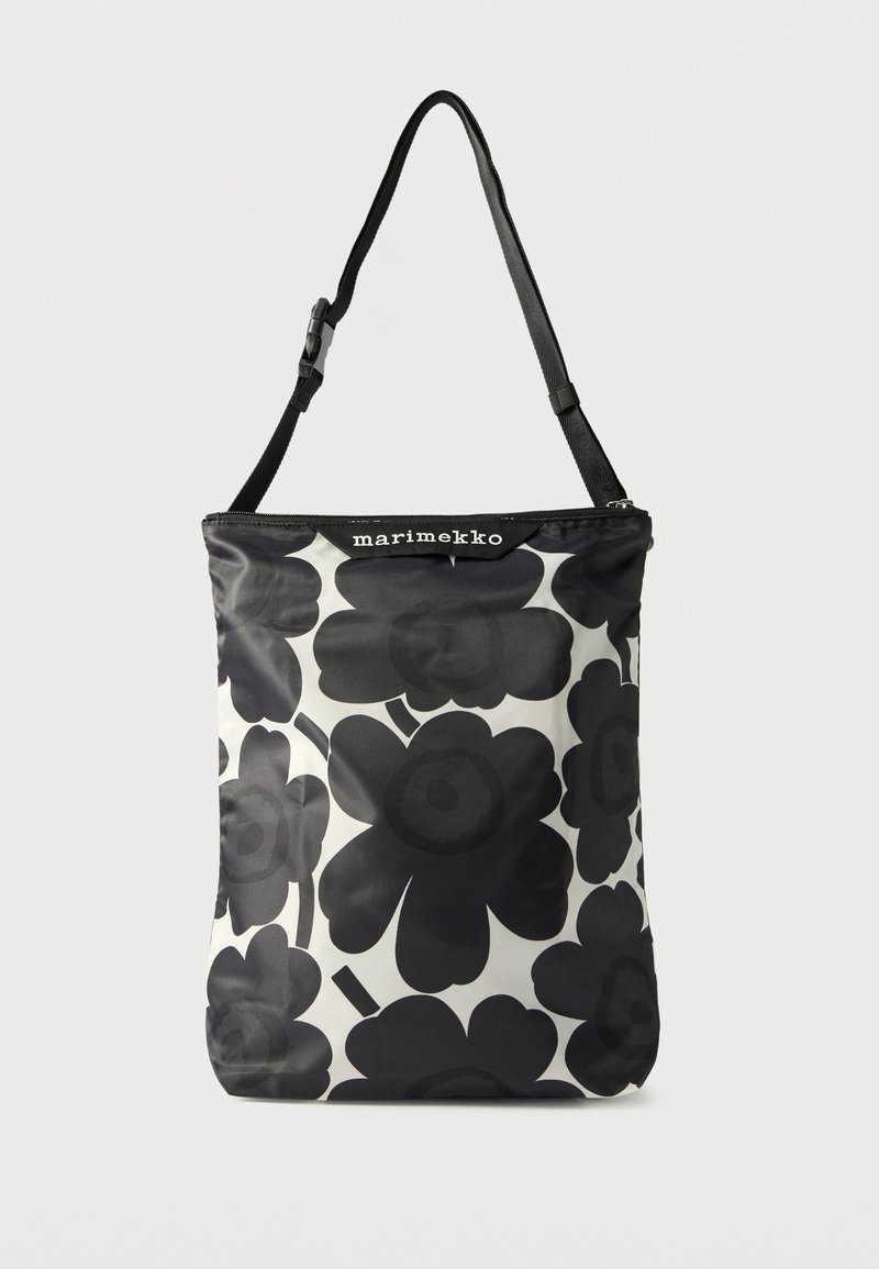 Sort og hvid blomsterprintet shoppingtaske lavet af blankt materiale med en øverste lynlås og en sort justerbar rem. Brandlogo er synligt øverst.