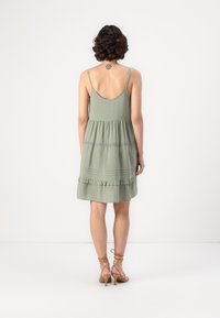 Πράσινο, αμάνικο φόρεμα με tiered σχεδίαση, που διαθέτει ραμμένο στρίφωμα και διακριτές ραφές. Το ύφασμα φαίνεται ελαφρύ και υβριδικό.