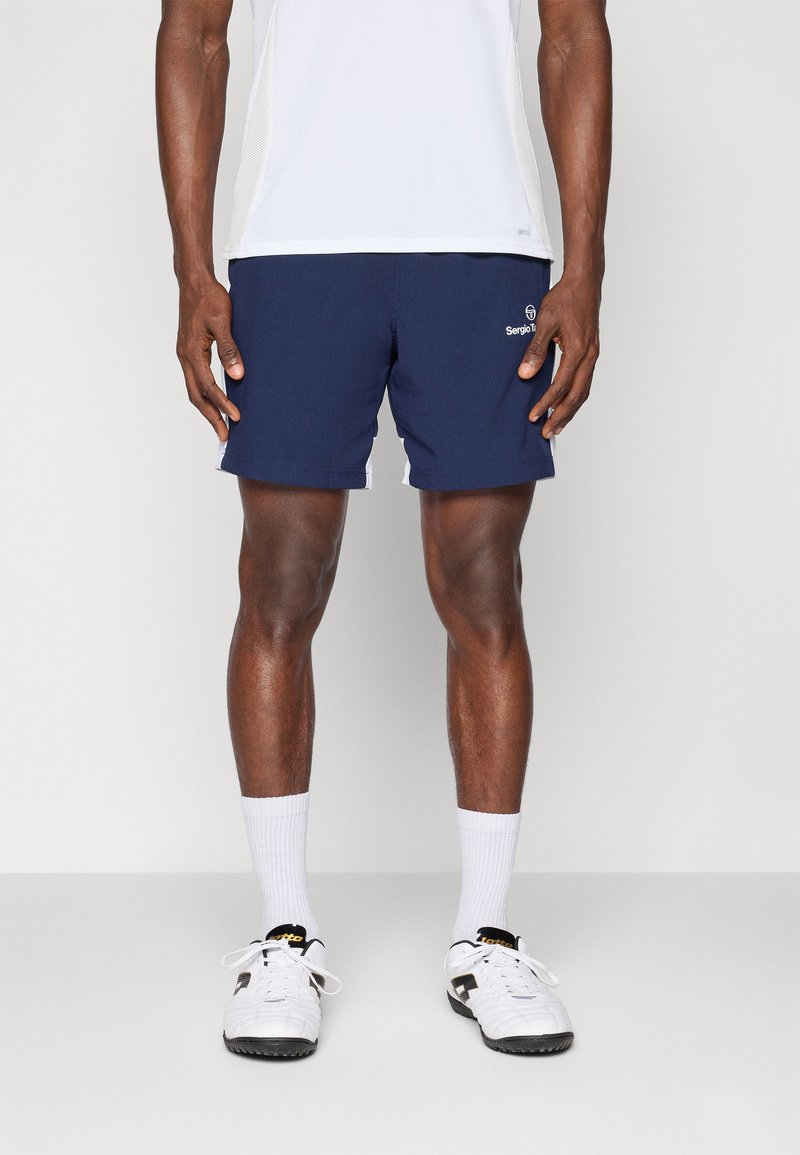Marineblauwe sportshorts met een gladde textuur, voorzien van een klein logo aan de voorkant, zijstrepen en een ontspannen pasvorm. Gecombineerd met witte sokken en schoenen.
