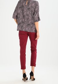 Top grigio con motivo floreale e apertura a chiave sul retro, abbinato a pantaloni bordeaux attillati e scarpe nere con tacco alto.