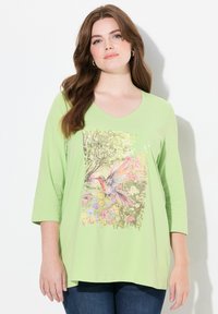 Lichtgroene, lange mouwen t-shirt met een levendige bloemen- en kolibriprint aan de voorkant. V-hals ontwerp. Zacht, rekbaar materiaal.