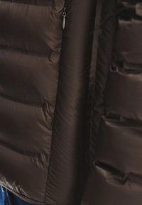 Gros plan d'une veste matelassée noire avec une fermeture éclair visible sur le côté gauche.