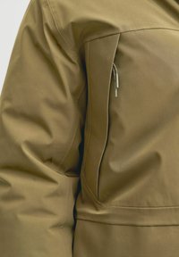 Tamsiai žalia pūkinė striukė su lygiu paviršiumi, turinti užtrauktuką priekinėje kišenėje ir struktūrizuotą, šiek tiek prigludusį dizainą.