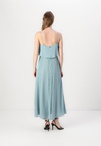 Maxi obleka v svetlo modri barvi, ki se ponaša z večplastnim dizajnom, nežnimi čipkastimi panneaux, tankimi naramnicami in podrobnostjo z gumbi na hrbtu.