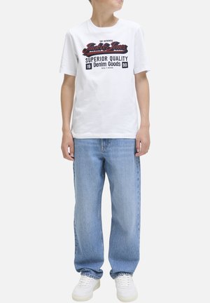 T-shirt en coton blanc avec texte imprimé en noir et rouge, assortie à un jean en denim bleu clair et des baskets blanches. Design simple, coupe décontractée.