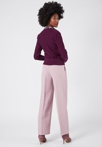 Lila stickad tröja med diamantmönster, rosa byxor och matchande klackar. Kragen har blommiga detaljer. Slät och skräddarsydd passform.