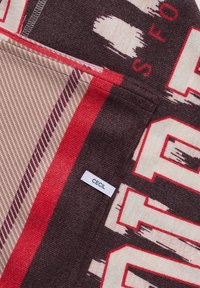 Gros plan d'un tissu avec des rayures rouges, beige et brun foncé et des lettres en bloc, avec une petite étiquette blanche portant le texte "CECIL".