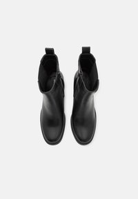 Paire de bottines en cuir noir avec fermetures éclair latérales et languettes, vues du dessus sur fond blanc.
