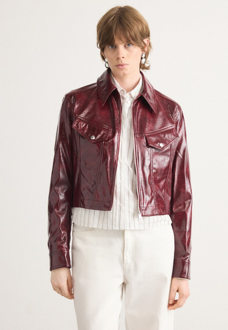 Burgundy faux leather cropped jacket with a classic collar, two chest pockets, and silver hardware details. Smooth texture with subtle sheen.