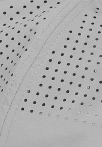 Gros plan sur un tissu gris clair avec des perforations rondes petites et uniformément espacées, et des coutures visibles le long d'une couture.