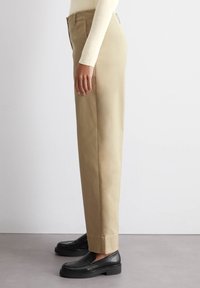 Beige broek met een rechte pasvorm, gemaakt van gladde stof. Heeft een platte voorkant en zijzakken, in combinatie met zwarte instappers.
