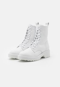Weiße Leder-Ankle-Boots mit einem klobigen Absatz, die über eine Schnürung, eine robuste Gummisohle und eine Schlaufe zum leichteren Anziehen verfügen.