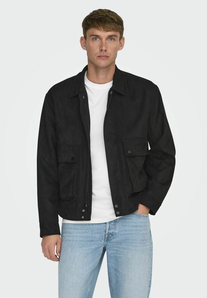 Svart mockajacka med två framfickor, tryckknappar och dragkedja framtill. Bärs över en vit t-shirt och ljusblå jeans.