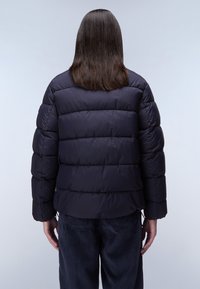 Navyblå pufferjacka med horisontell quiltning, texturerad tyg, elastiska manschetter och dragsko i nederkant. Buren över mörka manchesterbyxor.