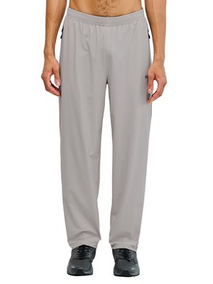 Mann trägt hellgraue locker sitzende Jogginghose mit elastischem Bund und schwarze Sneaker, steht vor weißem Hintergrund.