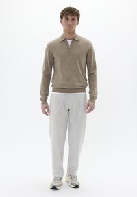 Sweater de punto beige con cremallera y cuello polo, combinado con pantalones de traje gris claro con pliegues y zapatillas multicolores. Texturas suaves en toda la prenda.