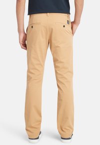 Pantaloni in cotone beige con un design a taglio dritto, dotati di tasche posteriori con bottoni e di una piccola etichetta del marchio sul lato destro.