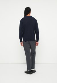 Pull en tricot bleu marine avec un col rond, associé à un pantalon gris et des chaussures noires. Texture visible à l'arrière du pull.