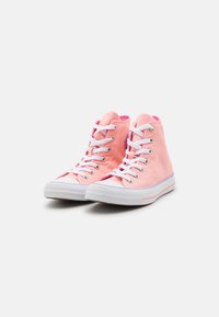 Pár růžových vysokých plátěných tenisek s bílou gumovou podrážkou a bílými tkaničkami na jednobarevném bílém pozadí.