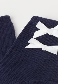 Námořnické bezprstové rukavice vyrobené z ribovaného pleteného materiálu, s dvěma bílými saténovými mašlemi jako akcenty na manžetě. Textura je měkká na dotek.