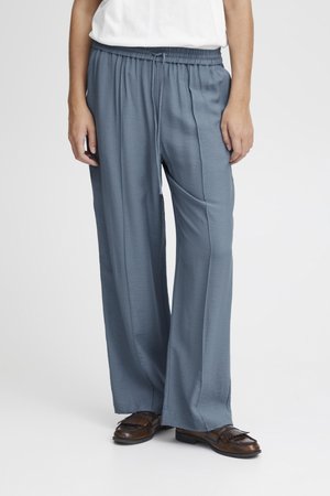 Pantalons larges bleu clair en tissu lisse avec une taille élastique et un cordon de serrage. Assortis à des mocassins marron foncé.