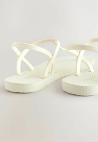 Weiße Flip-Flops mit strukturierten Sohlen und übereinanderliegenden Riemen. Glattes, leichtes Gummimaterial. Geformtes Fußbett für Komfort.