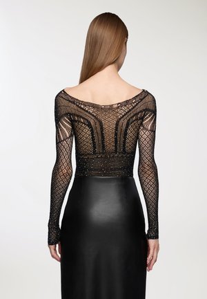 Top in pizzo nero con maniche lunghe, caratterizzato da un motivo a griglia e decorazioni sparse, abbinato a una gonna aderente in pelle nera.