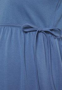 Vestido azul com parte de cima canelada e saia franzida. Inclui um cós amarrado e textura de tecido suave.