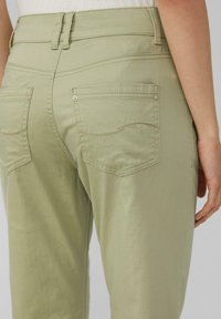 Jasnozielone spodnie o gładkiej fakturze, z dwoma tylnymi kieszeniami i subtelnymi detalami w szwach. Konstrukcja w talii na średnim poziomie.