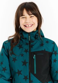 Tirkizna zimska jakna s crnim uzorkom zvijezda, s patentnim zatvaračima i akcentom s logotipom. Ima visoki ovratnik i podesivu kapu. Izrađena od izdržljivog materijala.