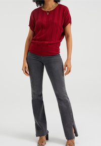 Červený žebrovaný pletený top spárovaný se šedými zvonovými džíny se bočními rozparky. Oblečení doplňují sandály na tenkém podpatku.