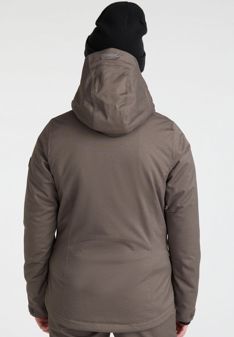 Braune isolierte Jacke mit Kapuze, strukturiertem Stoff und Logodetail auf dem Rücken. Begleitet von einer schwarzen Strickmütze.