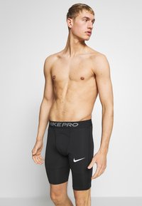 Barbent man med kort blont hår ser åt höger, iförd svarta Nike Pro kompressionsshorts mot en enkel bakgrund.