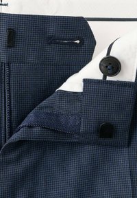 Zbliżenie na granatową i czarną kratkę na tkaninie z dziurką na guzik, czarnym guzikiem i ukrytym zamkiem błyskawicznym na ubraniu.